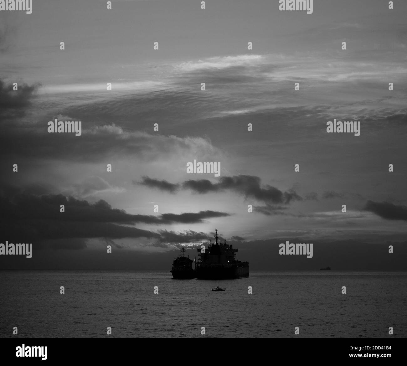 Sunrise from the sea with low clouds and backlit ships, black and white ...