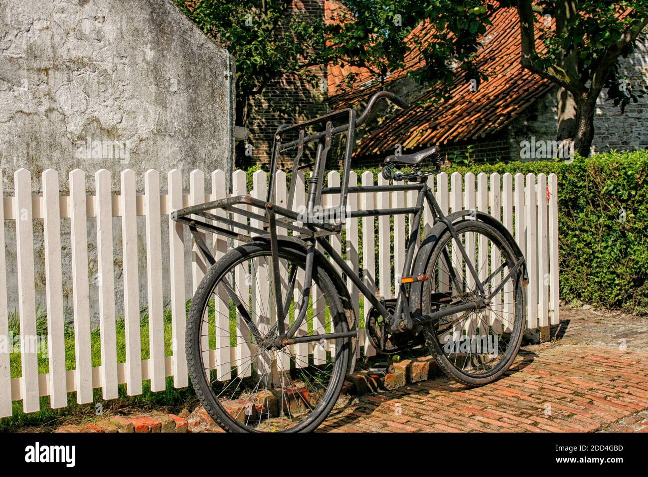 Old black bicycle standing against white picket fence in the Netherlands Stock Photo