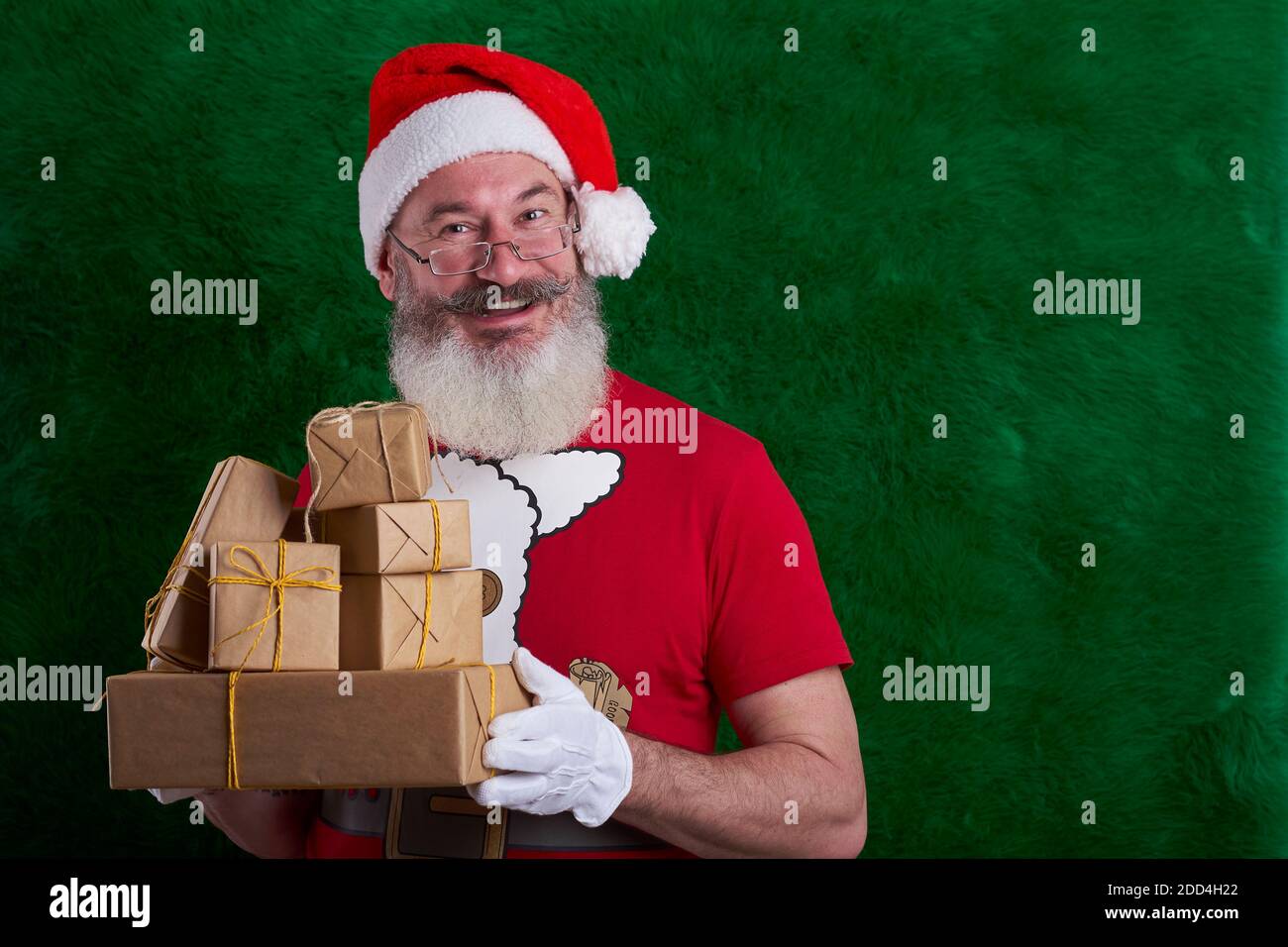 Mature bearded man wearing Santa hat with many gifts in hand, Santa smiling and looking at camera, copy space Stock Photo