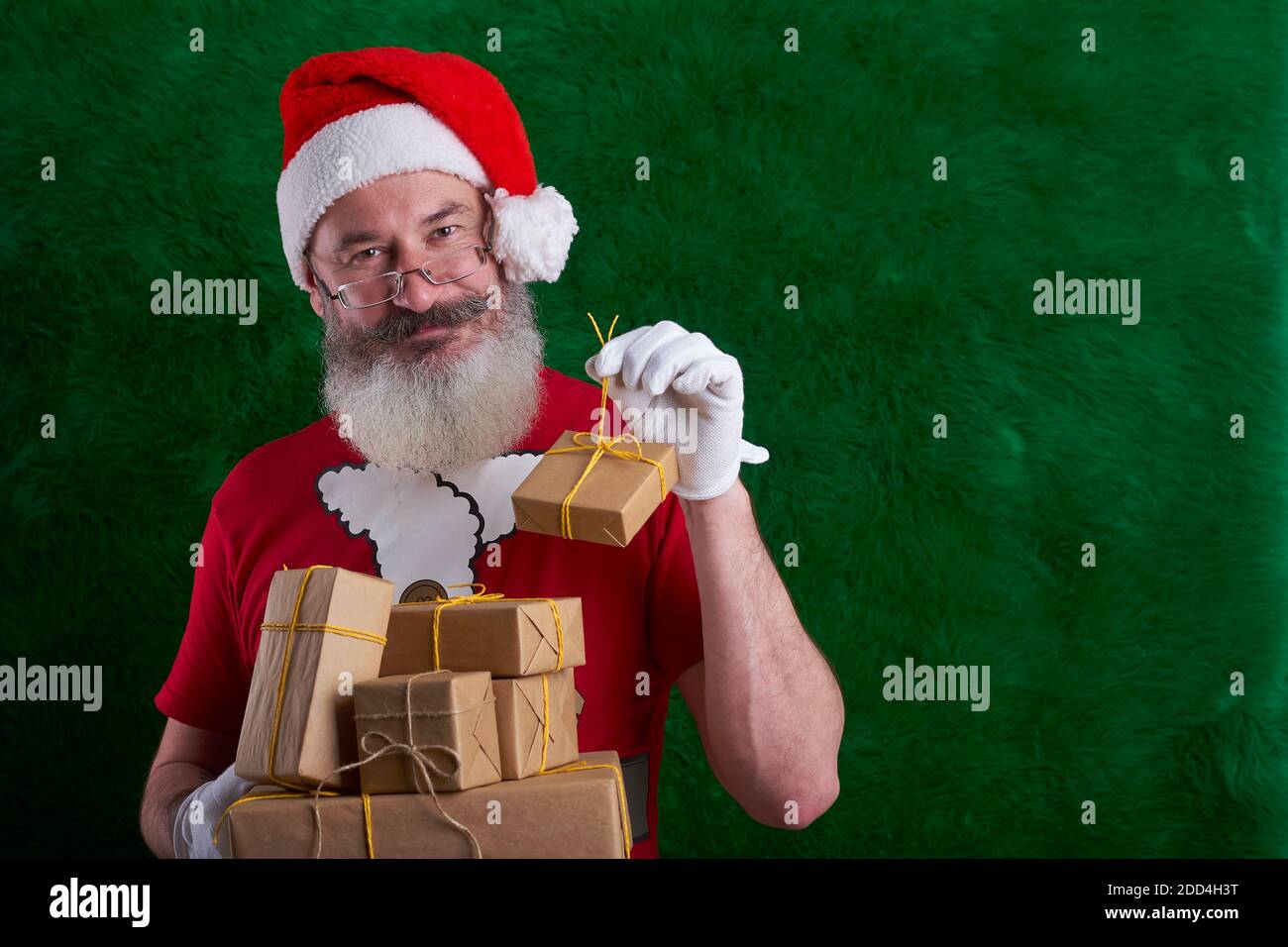 Mature bearded man wearing Santa hat with many gifts in hand, Santa smiling and looking at camera, copy space Stock Photo