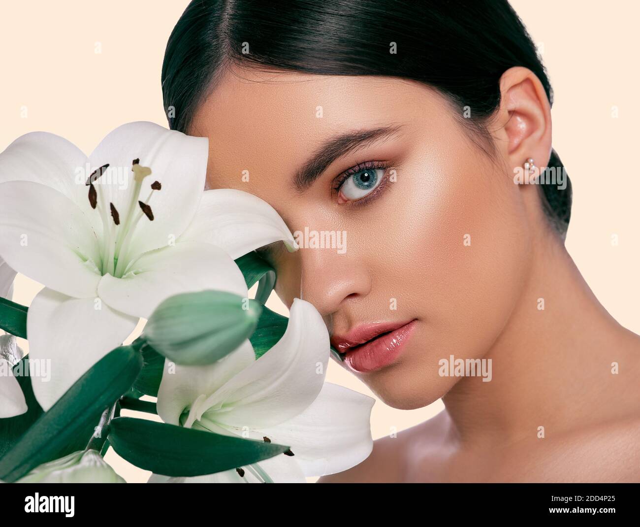 Skin care concept. Brunette woman with clean, fresh skin and lily flower near her face, on set sail champagne color background Stock Photo
