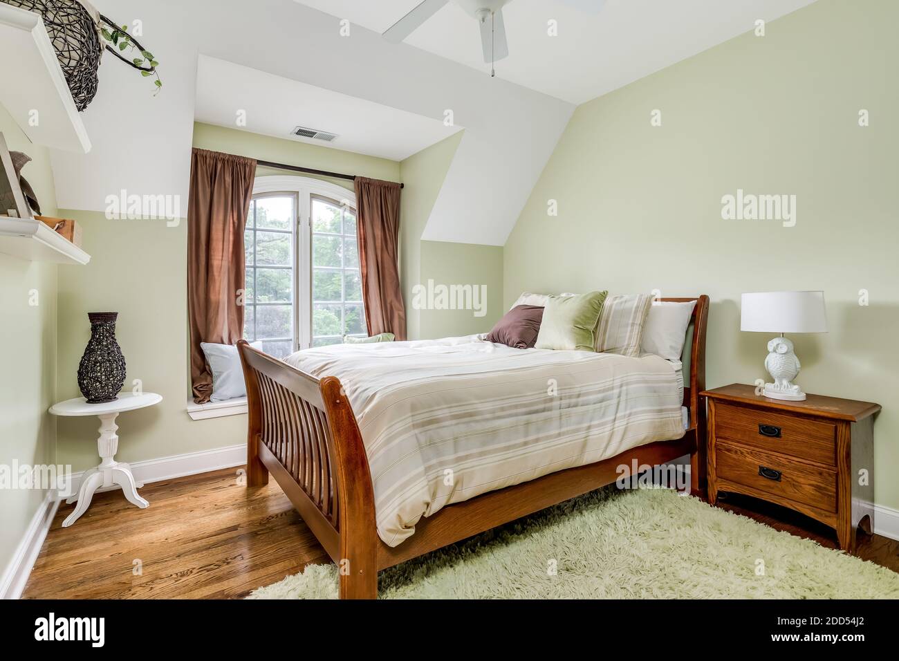 A cozy, light green room with a bed and natural wood furniture Stock