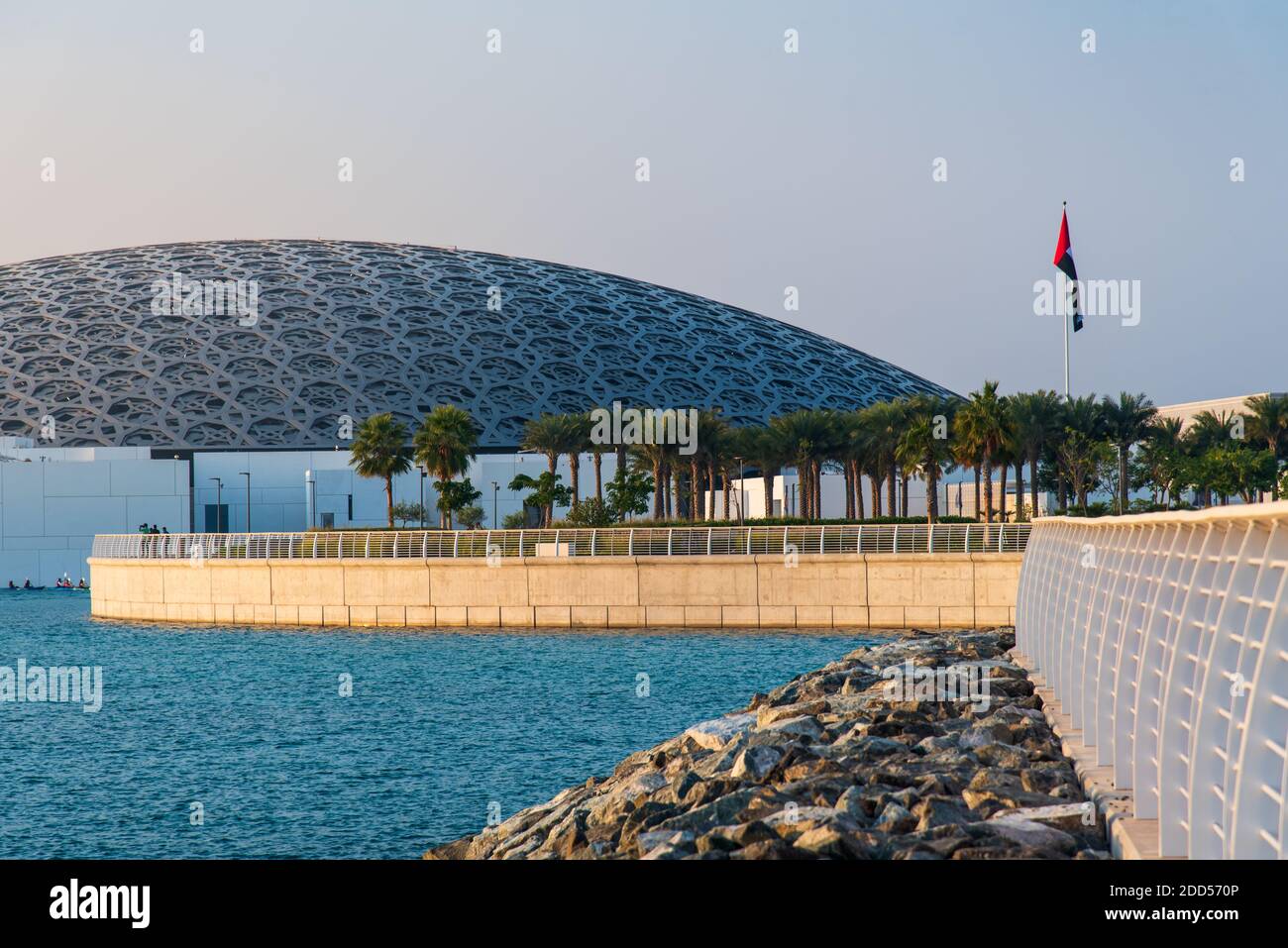 Abu Dhabi, United Arab Emirates - November 30, 2019: UAE flag and Louvre museum in Abu Dhabi exterior and entrance with characteristic architecture on Stock Photo