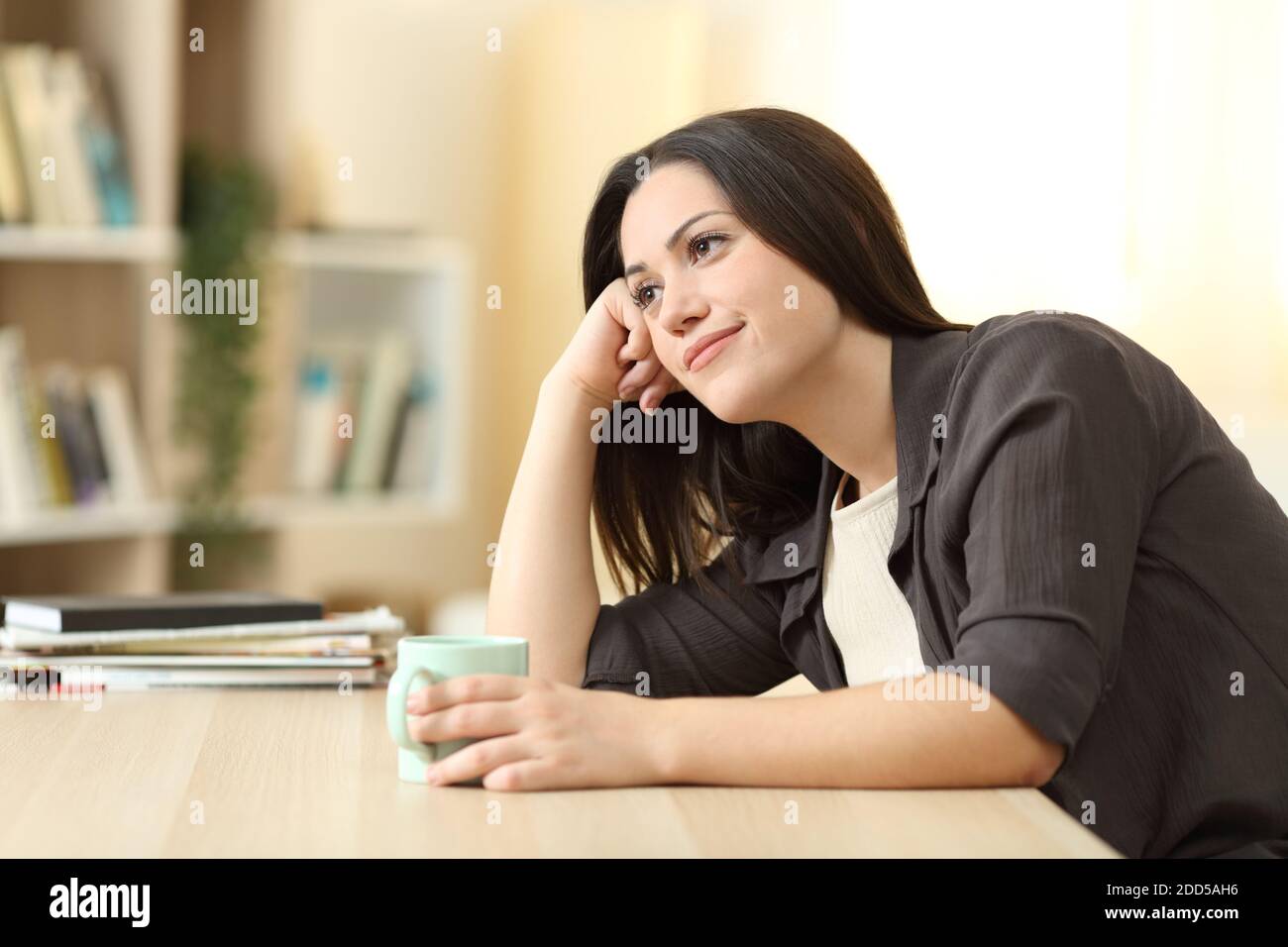 Pensive woman drinking coffee and thinking on a dek in the living room at home Stock Photo