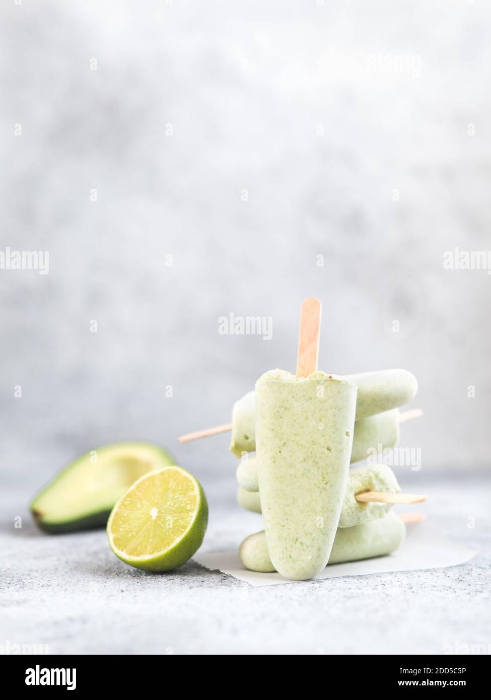 Homemade raw vegan avocado lime popsicle. Sugar-free, non-dairy green ice cream on gray cement textured background. Copy space. Ideas and recipes for healthy snack, dessert or smoothie. Vertical Stock Photo