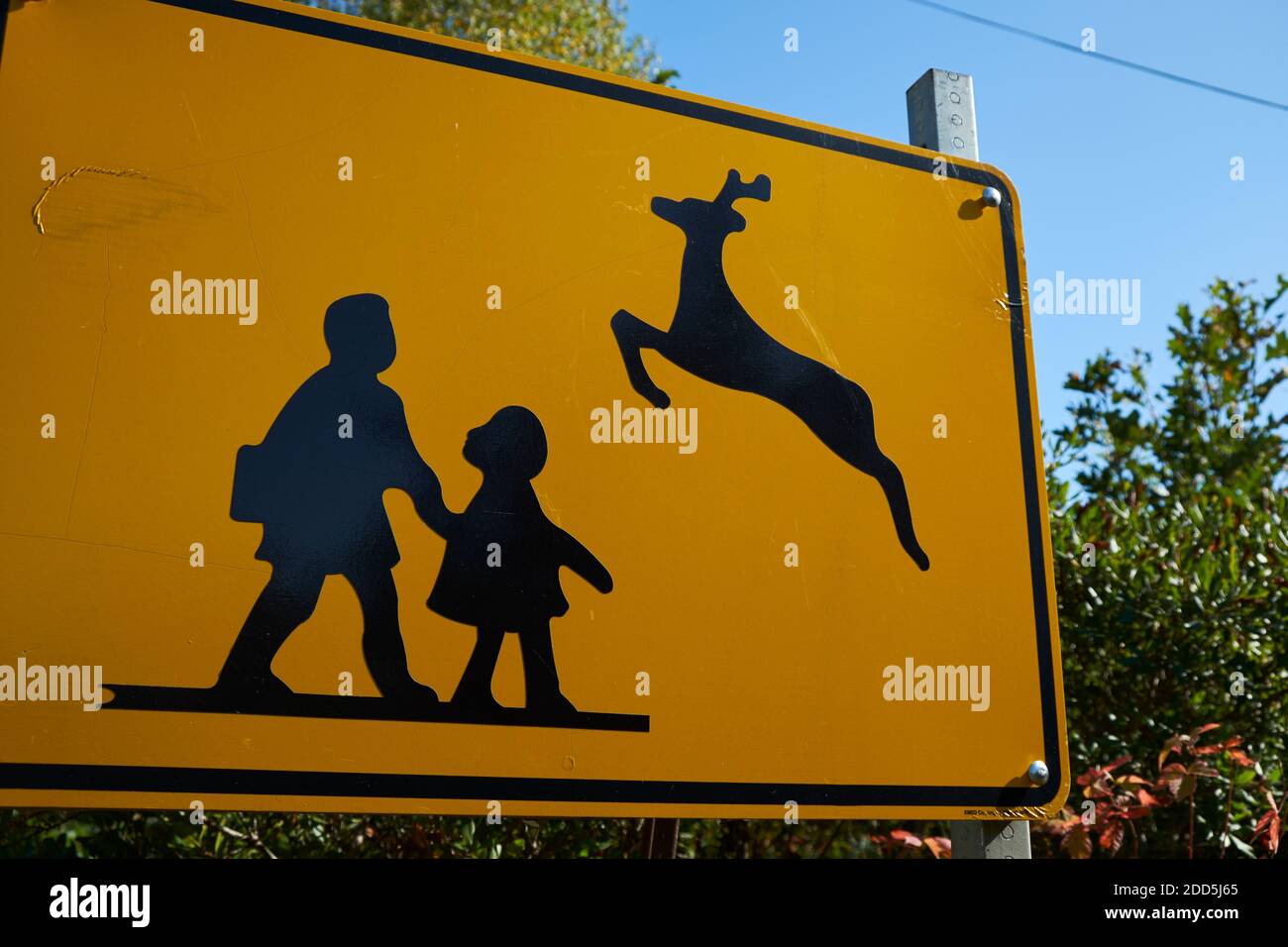 A yellow street warning sign with a funny juxtaposition of school children and jumping deer