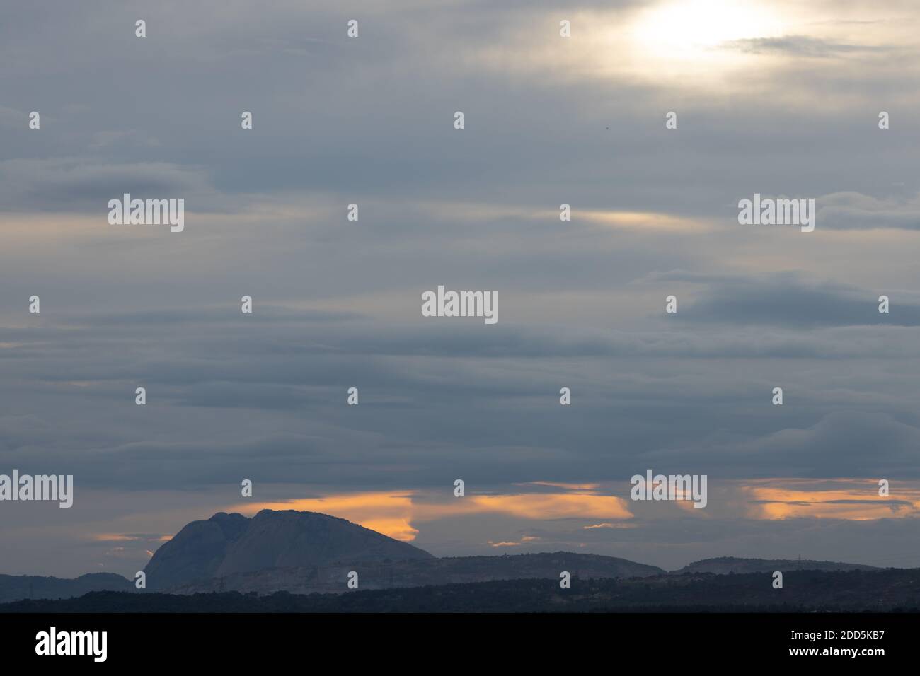 A Panoramic Silhouette of hills in the bottom with dark clouds in the horizon with orange sunlight  peeping through them Stock Photo