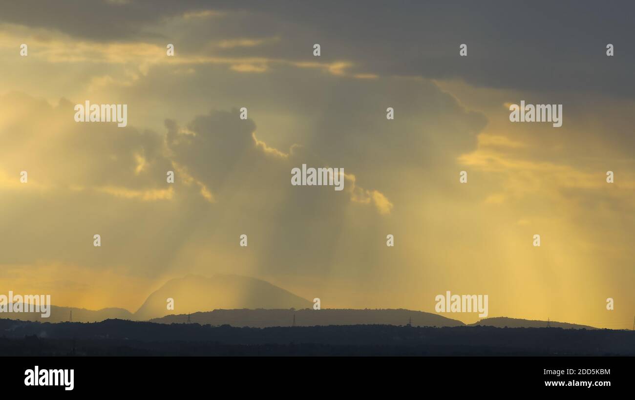Silhouette of a hills against beautiful golden hour light and beautiful clouds formation with rays of sunlight breaking Stock Photo