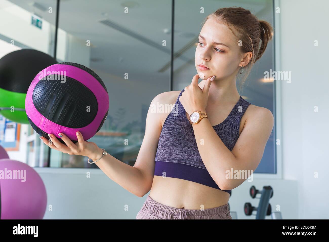 Young beautiful blond sporty girl  in a gym holds black pink med ball Stock Photo