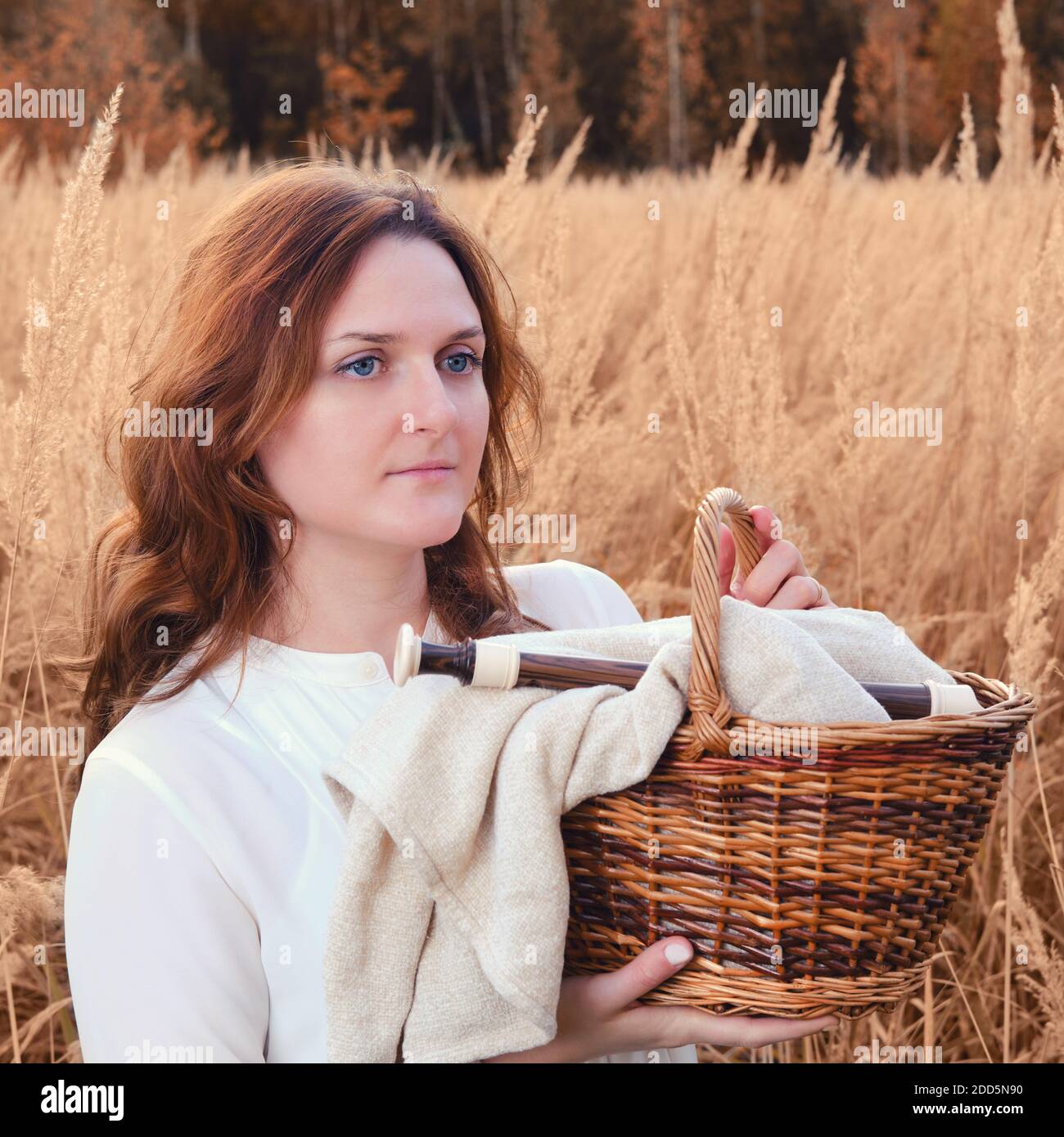 A woman with a basket and a musical instrument flute stands in autumn grass Stock Photo