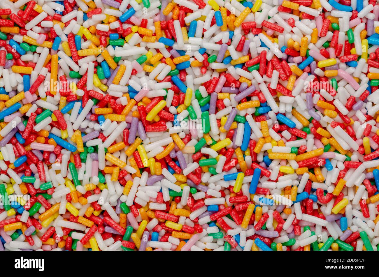 Rainbow sprinkles, background and surface. Rod-shaped colorful sugar sprinkles. Tiny candies in a variety of colors, used as decoration or topping. Stock Photo