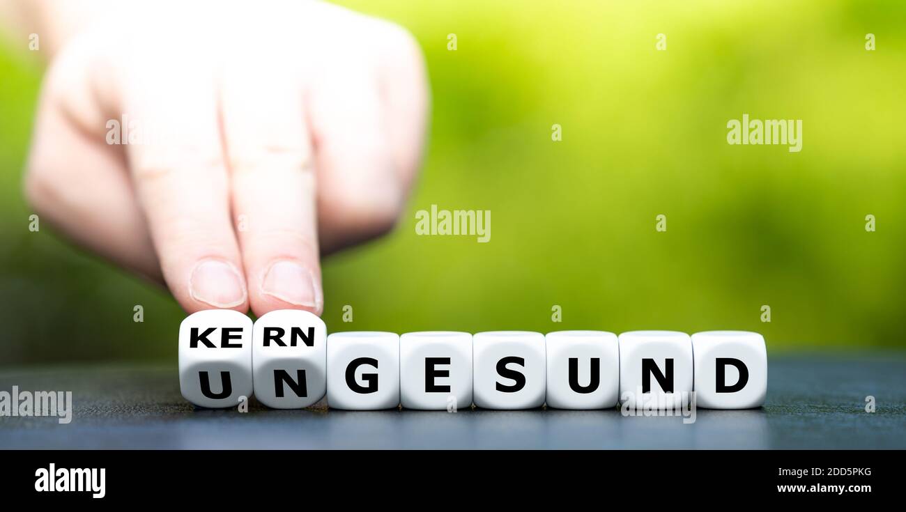 Hand turns dice and changes the German word 'ungesund' (unhealthy) to 'kerngesund' (healthy). Stock Photo