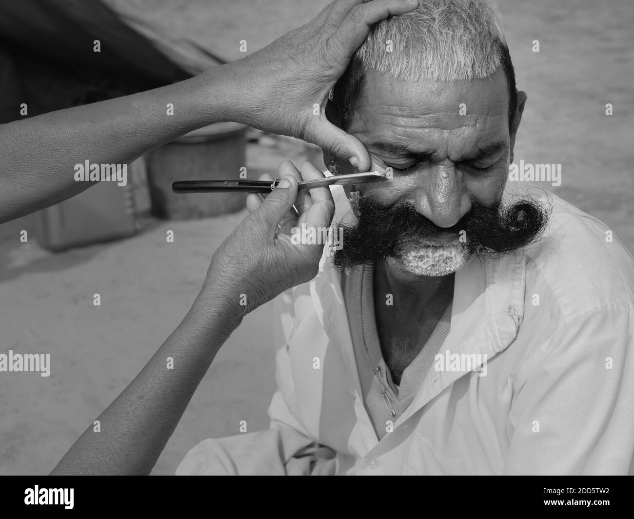 Man with long moustache receives shave and haircut by street barber using a cut throat razor in Pushkar, Rajasthan, India. Stock Photo