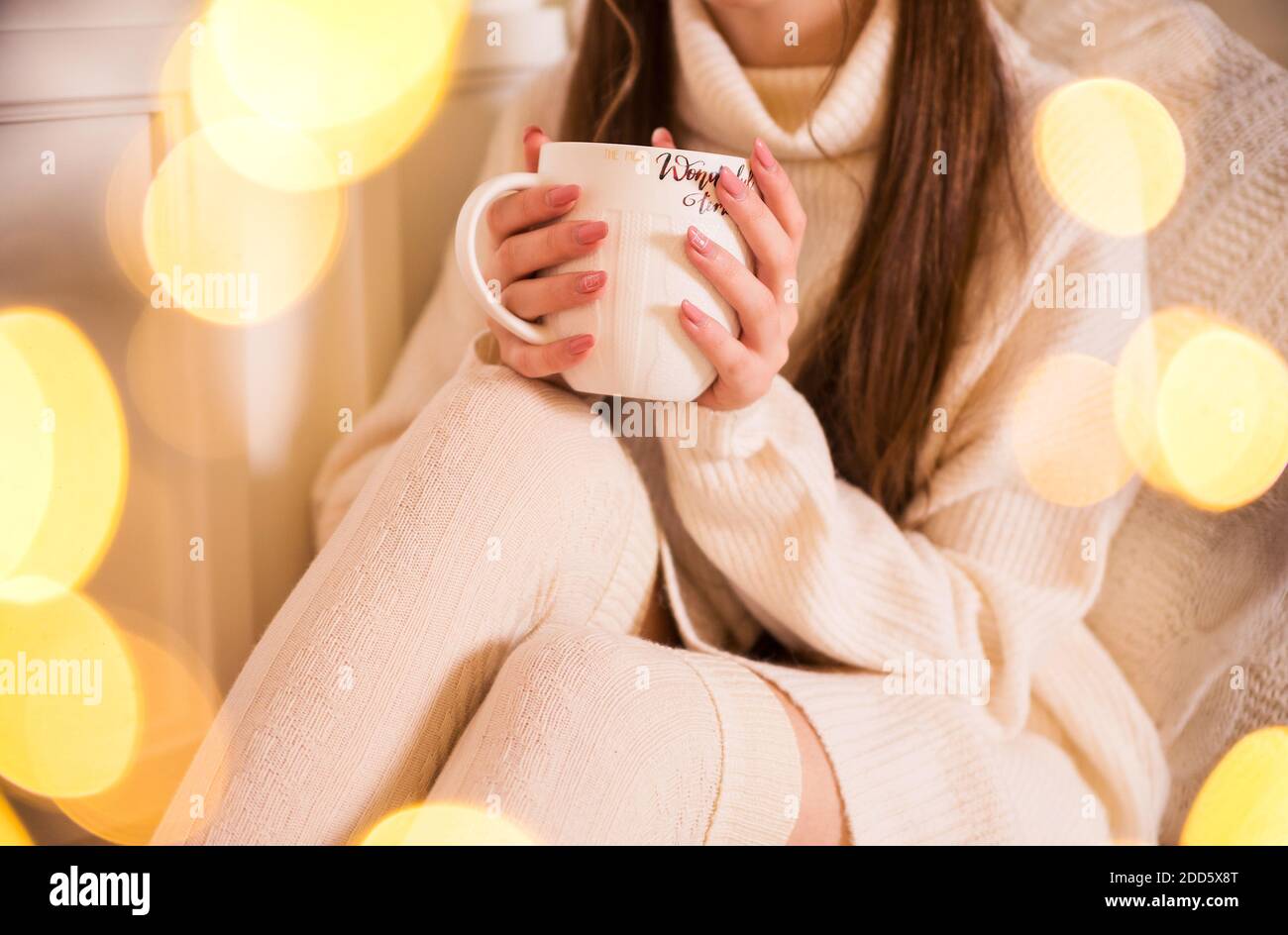 A girl in a white sweater and leggings holds a large white cup in her hands Stock Photo
