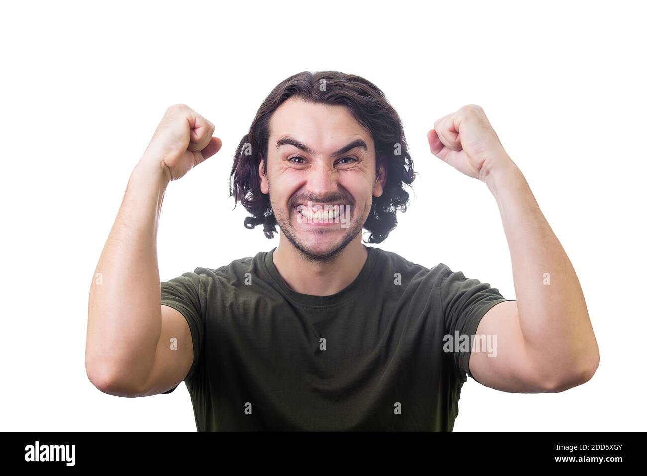 Pleased young man, long curly hair style, celebrates success hysterical and passionate. Guy keeps fists tight, raise hands up clenching teeth, isolate Stock Photo