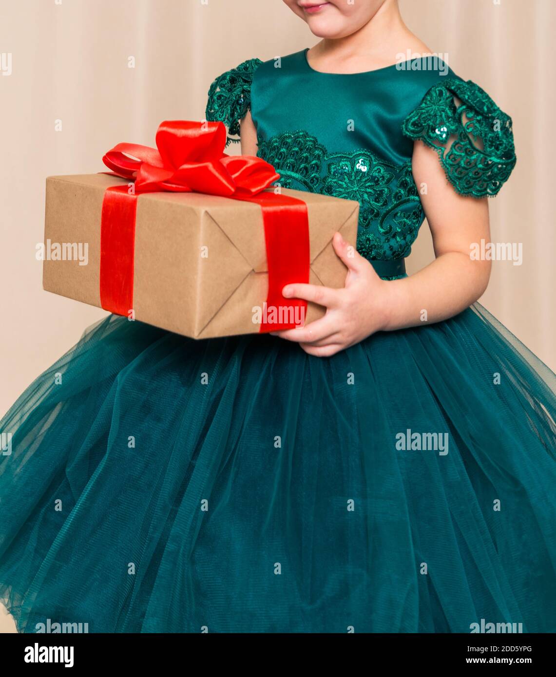 A girl in a chic green dress stands with a New Year's gift in her hands against the background of a New Year tree Stock Photo