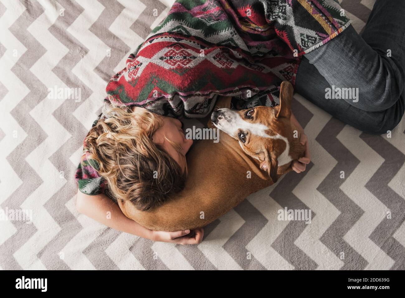 Woman lays down with a dog and hugs her. Emotional support, depression and stress relief with pets during lockdown and stay at home orders Stock Photo