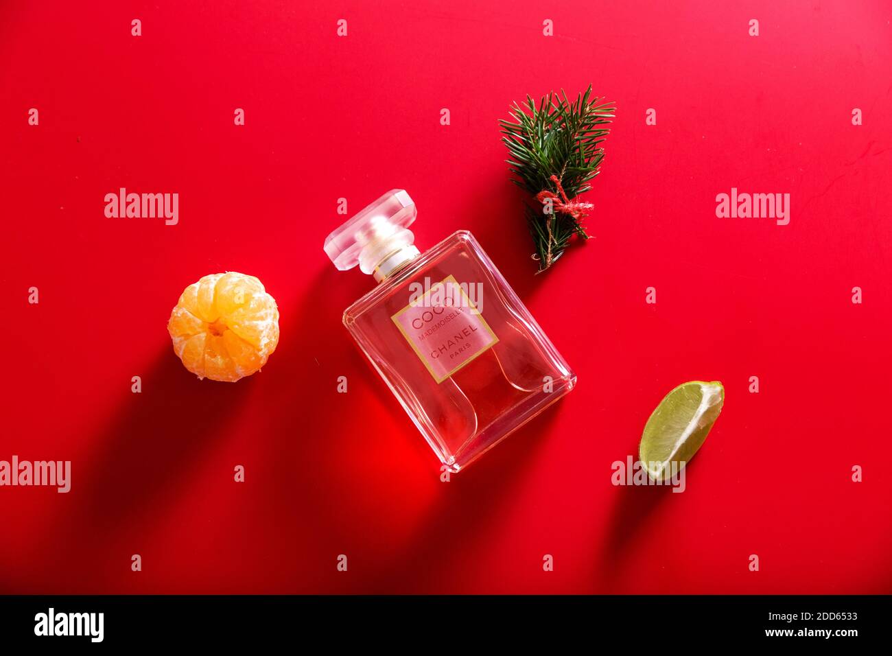 A bottle of perfume among the decor of Christmas tree branches, tangerine and lime on a red background Stock Photo
