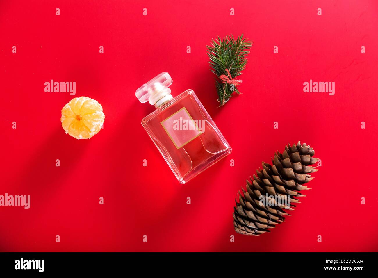 A bottle of perfume among the decor of Christmas tree branches, tangerine and cones on a red background Stock Photo