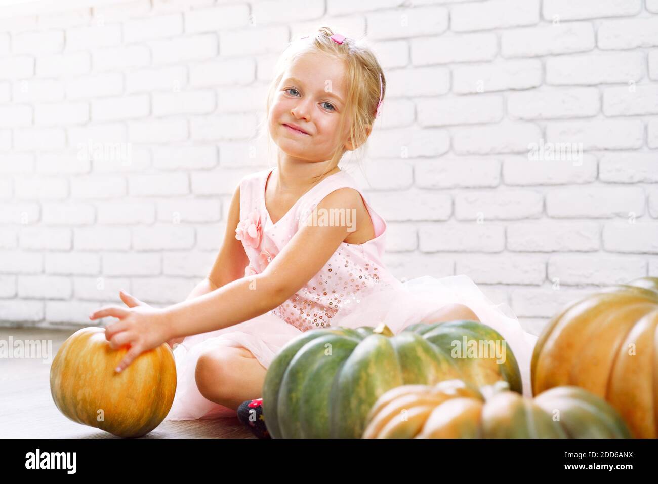Little girl in pink dress sitting on wooden floor and playing with pile ...