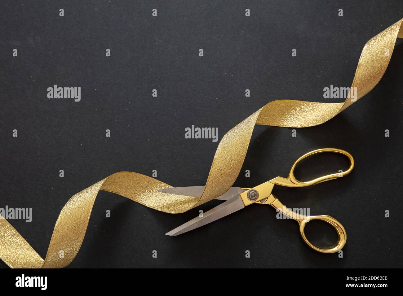 Grand opening. Gold scissors cutting golden silk ribbon, black background, top view. Invitation template, copy space Stock Photo