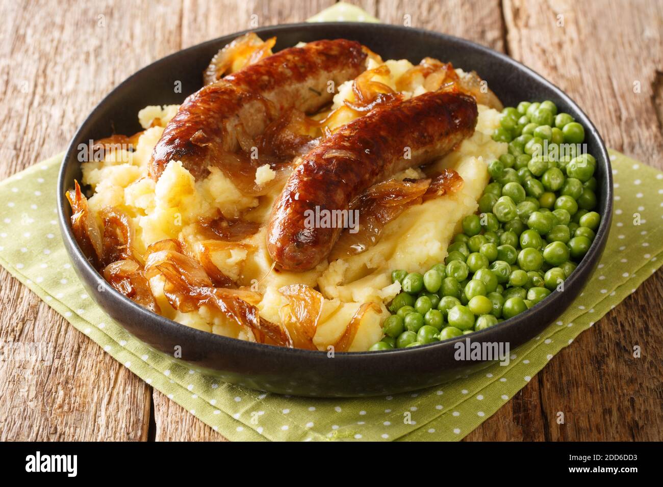 Traditional British cuisine fried sausages with mashed potatoes, onion gravy and green peas close-up in a plate on the table. horizontal Stock Photo