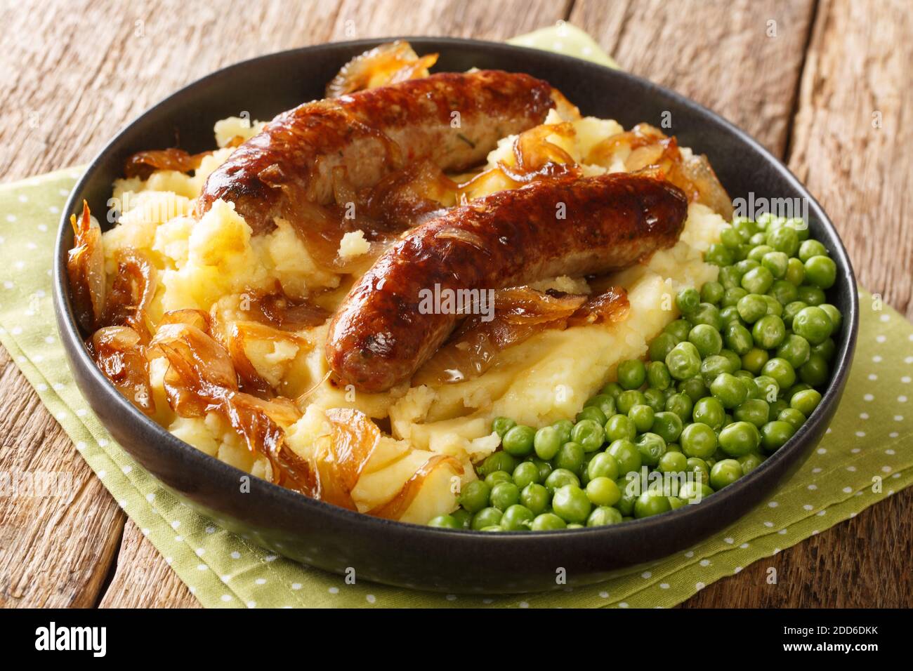 Tasty Bangers and Mash made of sausages served with mashed potatoes, green peas and onion gravy close-up in a plate on the table. Horizontal Stock Photo