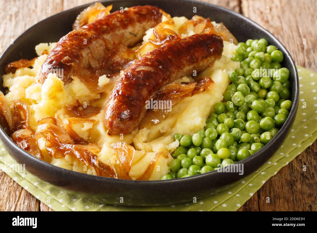 Fried sausages with mashed potatoes, onion gravy and green peas close-up in a plate on the table. horizontal Stock Photo