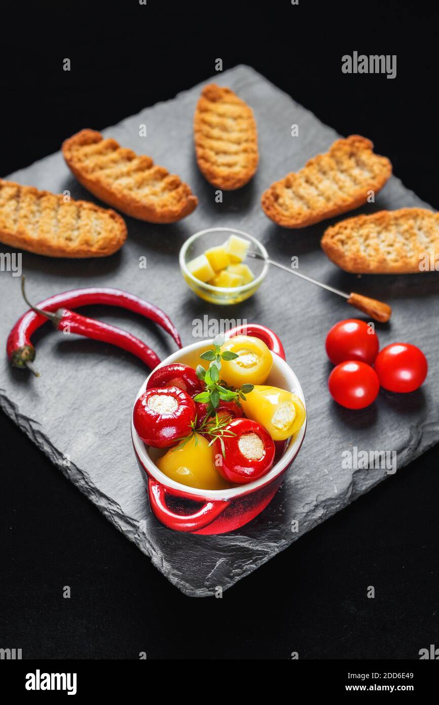 Tiny red and yellow hot peppers filled with cheese (Balkan delicacy) served with rusk, chilli peppers and cherry tomatoes (selective focus) Stock Photo