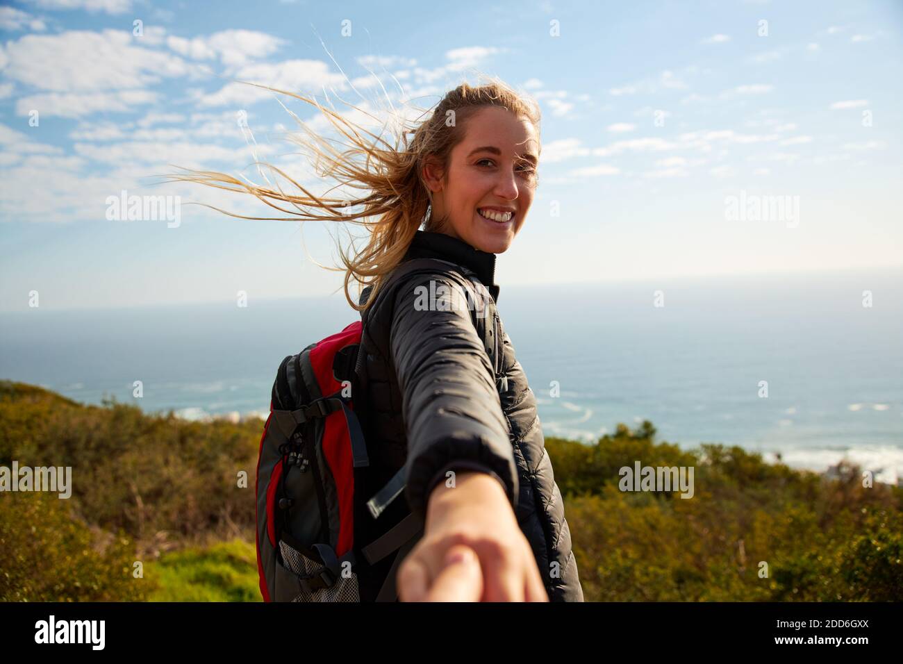 Point of view shot of active young woman hiking in countryside by sea encouraging off screen partner to follow her by holding his hand Stock Photo