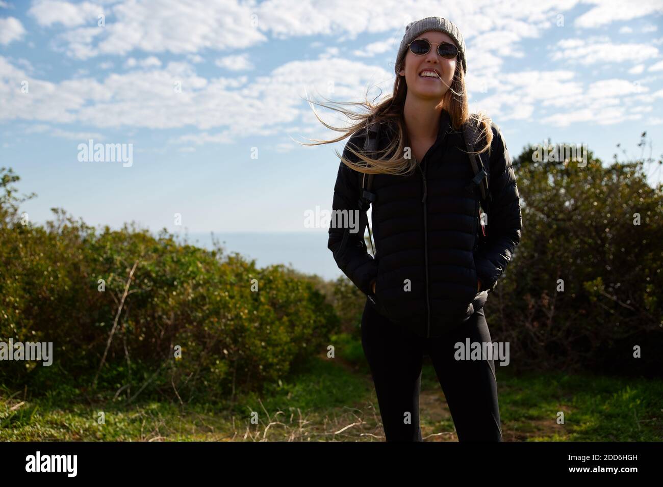 Young woman wearing sunglasses and beanie hat with backpack facing