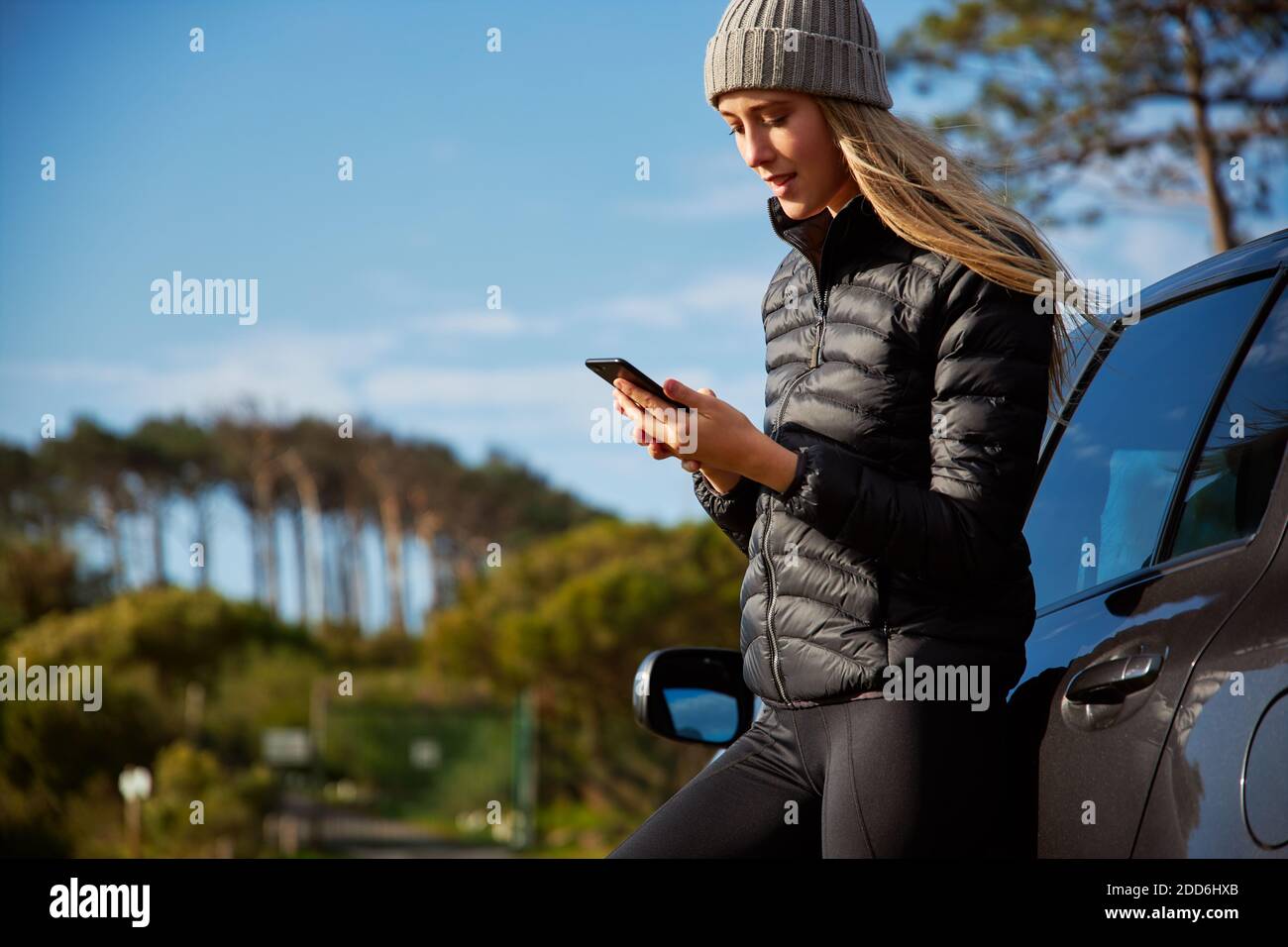 Young woman standing next to car which has broken down or she could be