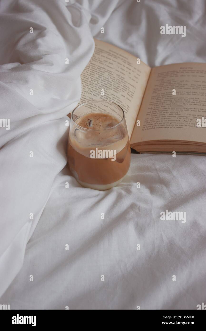 Close up iced coffee with ice cubes on it. White sheet accompanied by an open book. Minimalist aesthetic photography detail. Product Photography 2020. Stock Photo