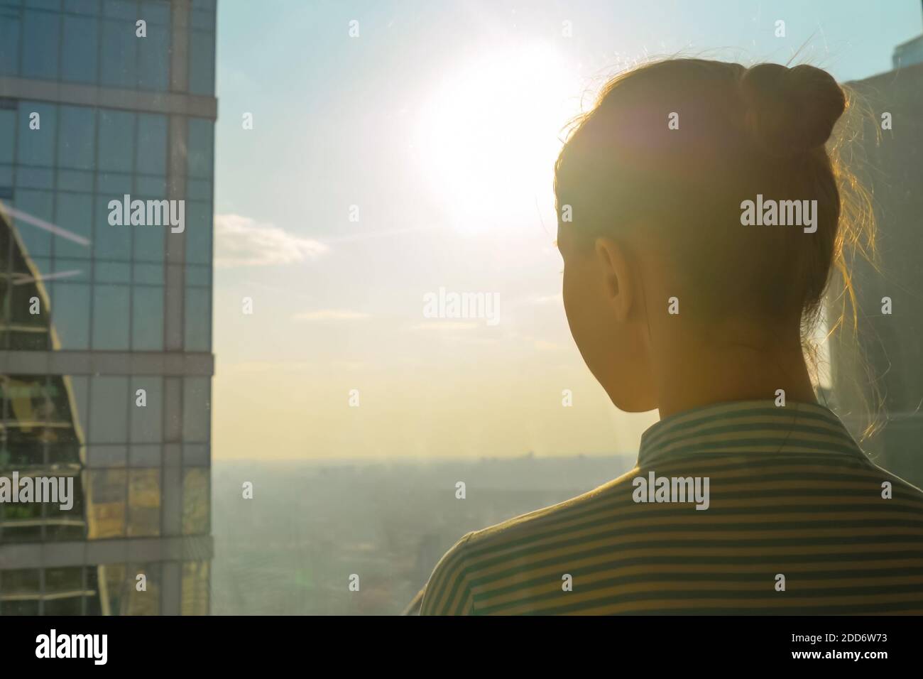 Back view of woman silhouette looking at cityscape through window of ...