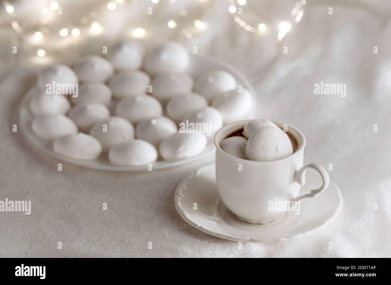 White cup of coffee with meringues on soft blanket. Bokeh lights on the background. Cozy winter still life. Stock Photo