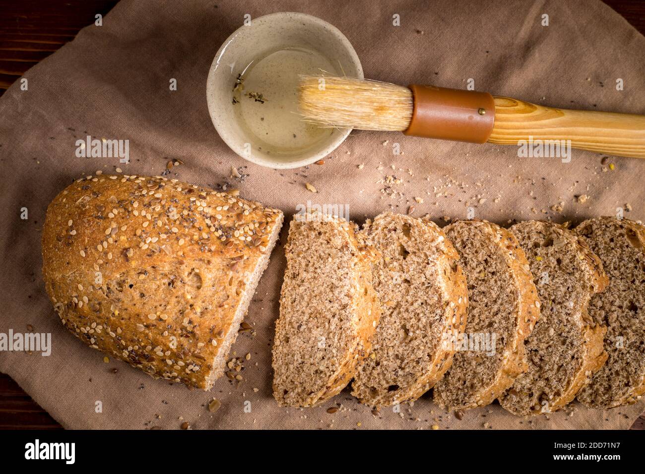 An overview of sliced seeded bread a brush and a cup of olive oil Stock