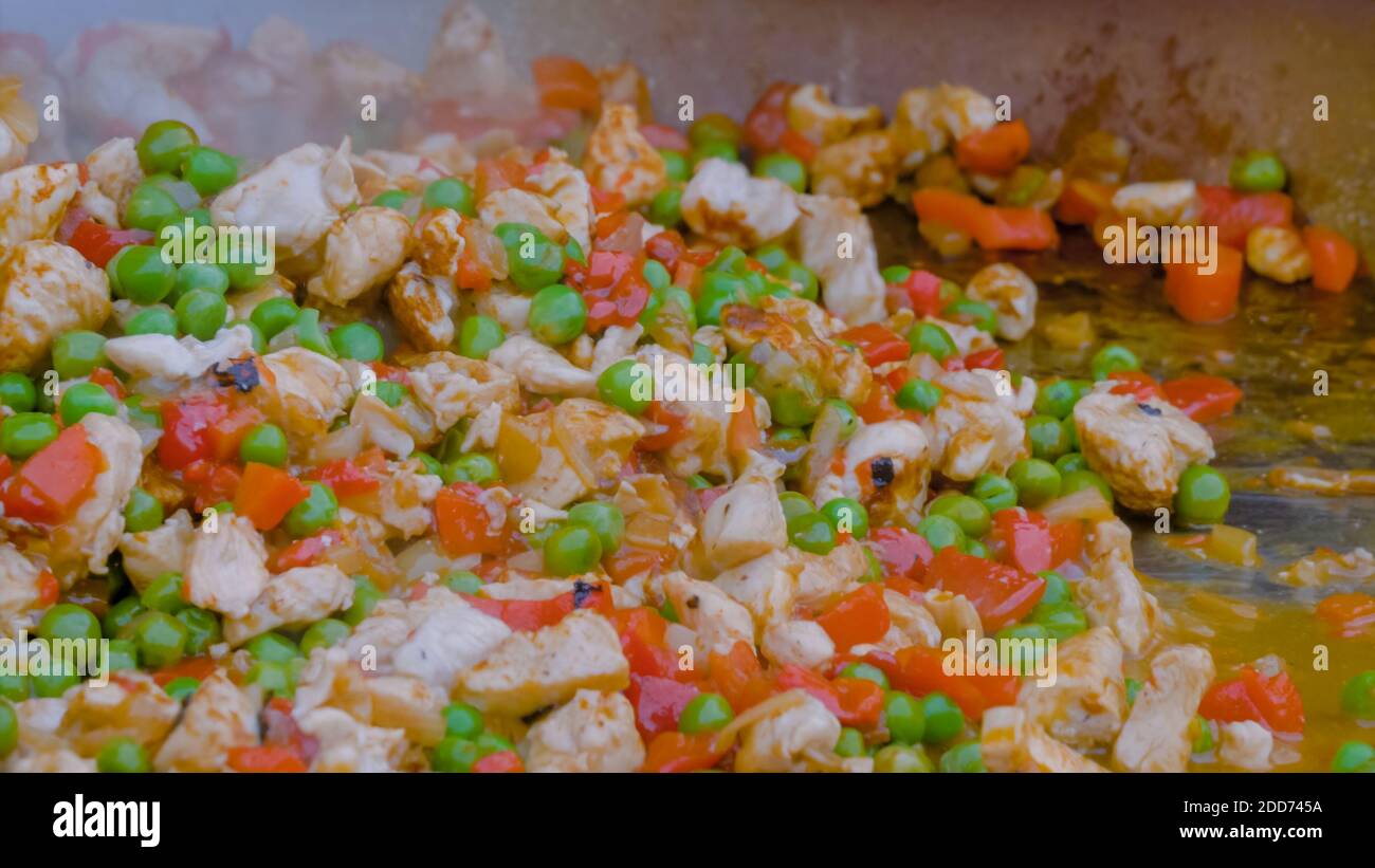 Process of cooking meat pieces, peppers, peas in huge wok - close up Stock Photo