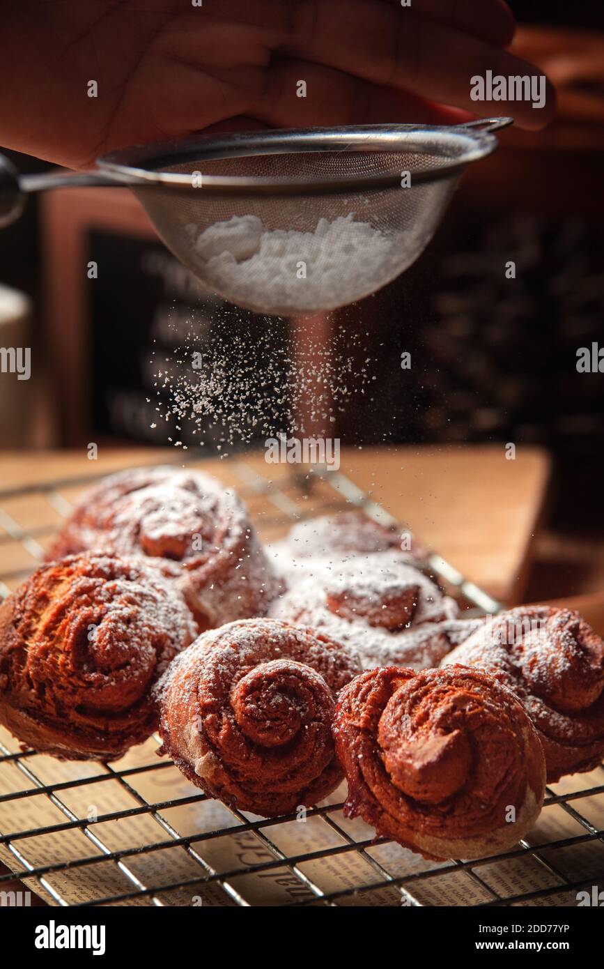Close Up view chef sprinkle icing sugar over the cinnamon rolls Stock Photo
