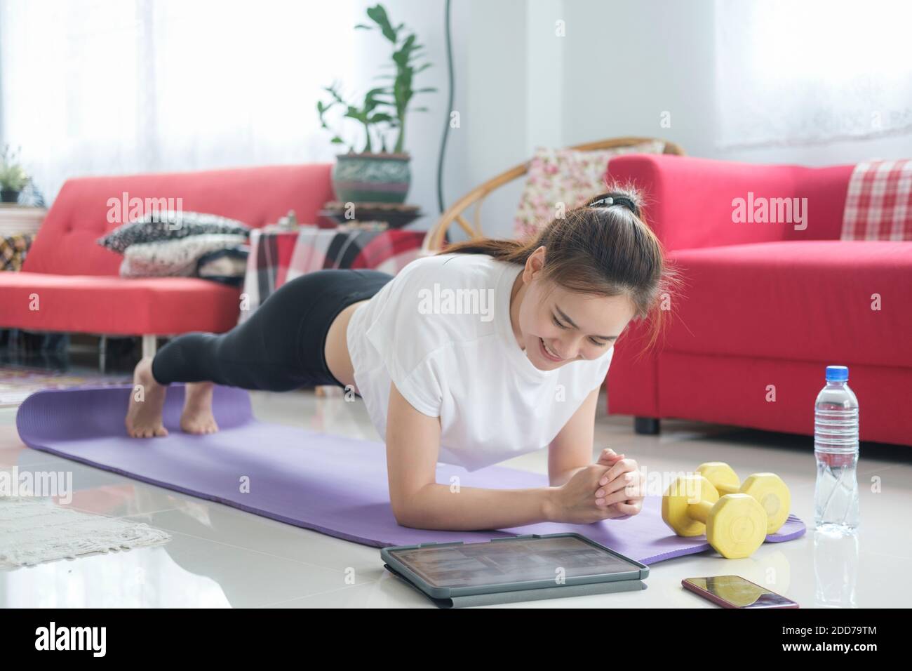 Fit woman doing yoga plank and watching online tutorials, training in living room. Stay at home life style. Stock Photo