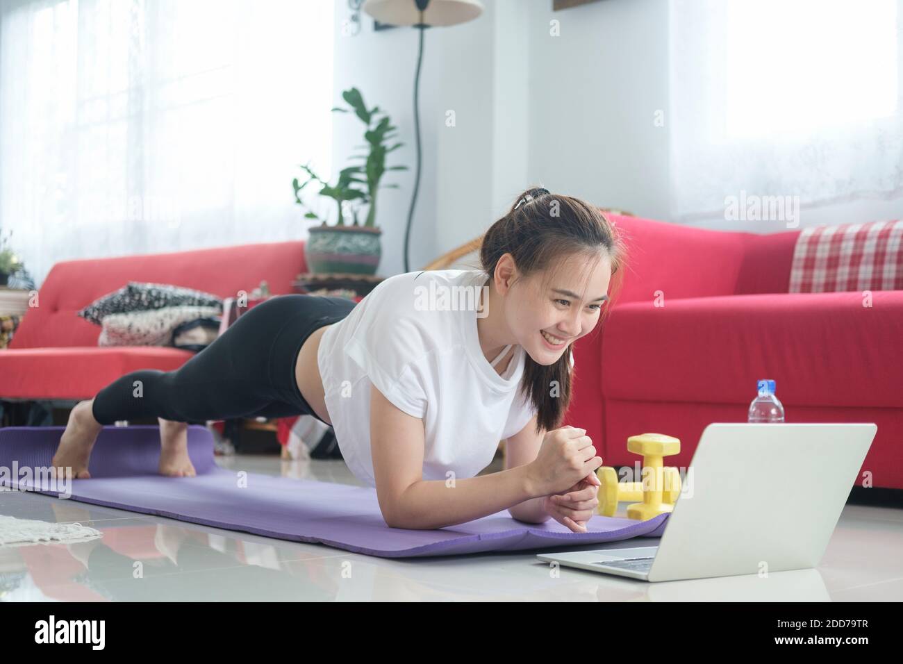 Fit woman doing yoga plank and watching online tutorials, training in living room. Stay at home life style. Stock Photo