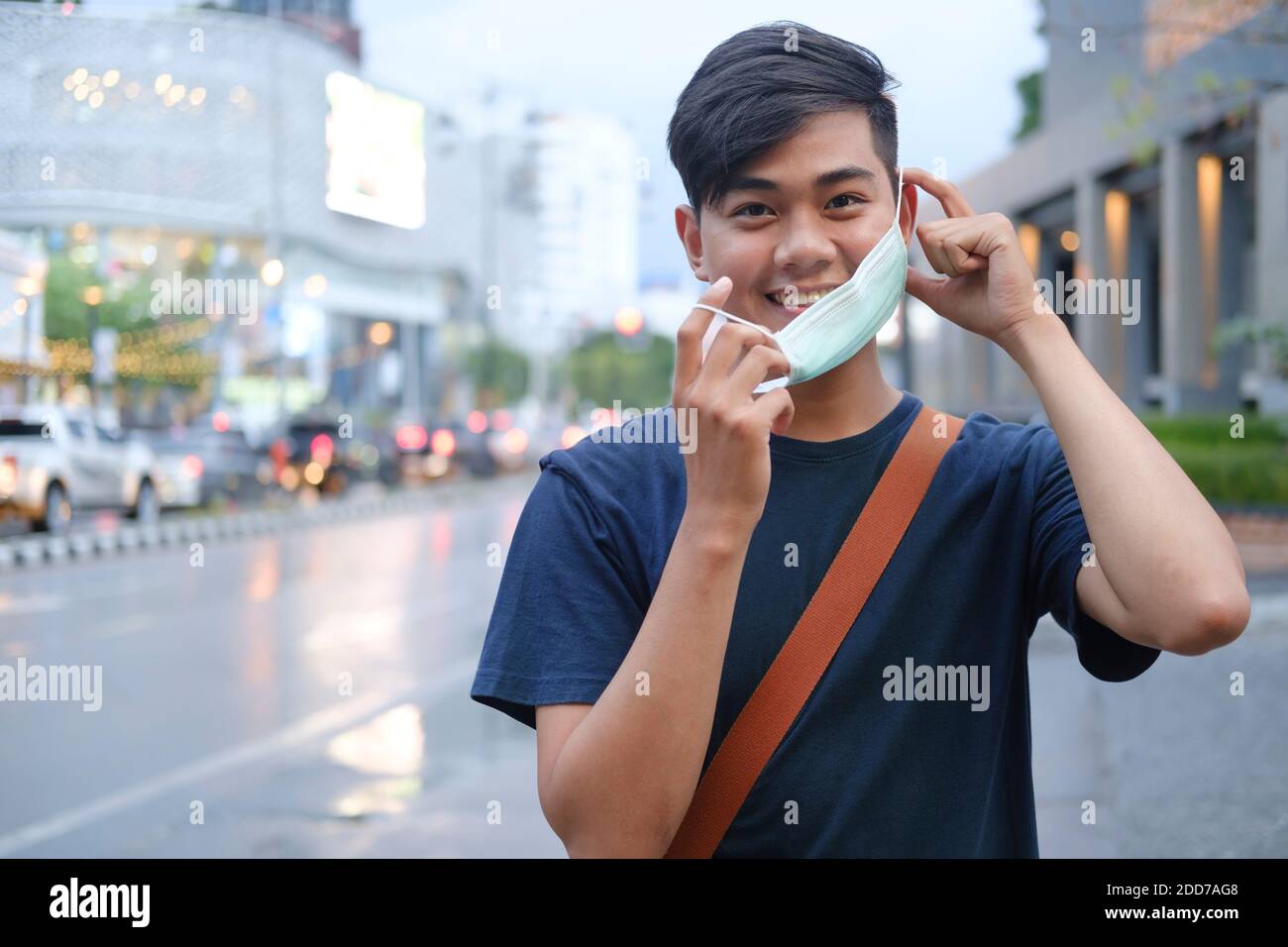 Young man during pandemic isolation at city. Removing mask from face ...