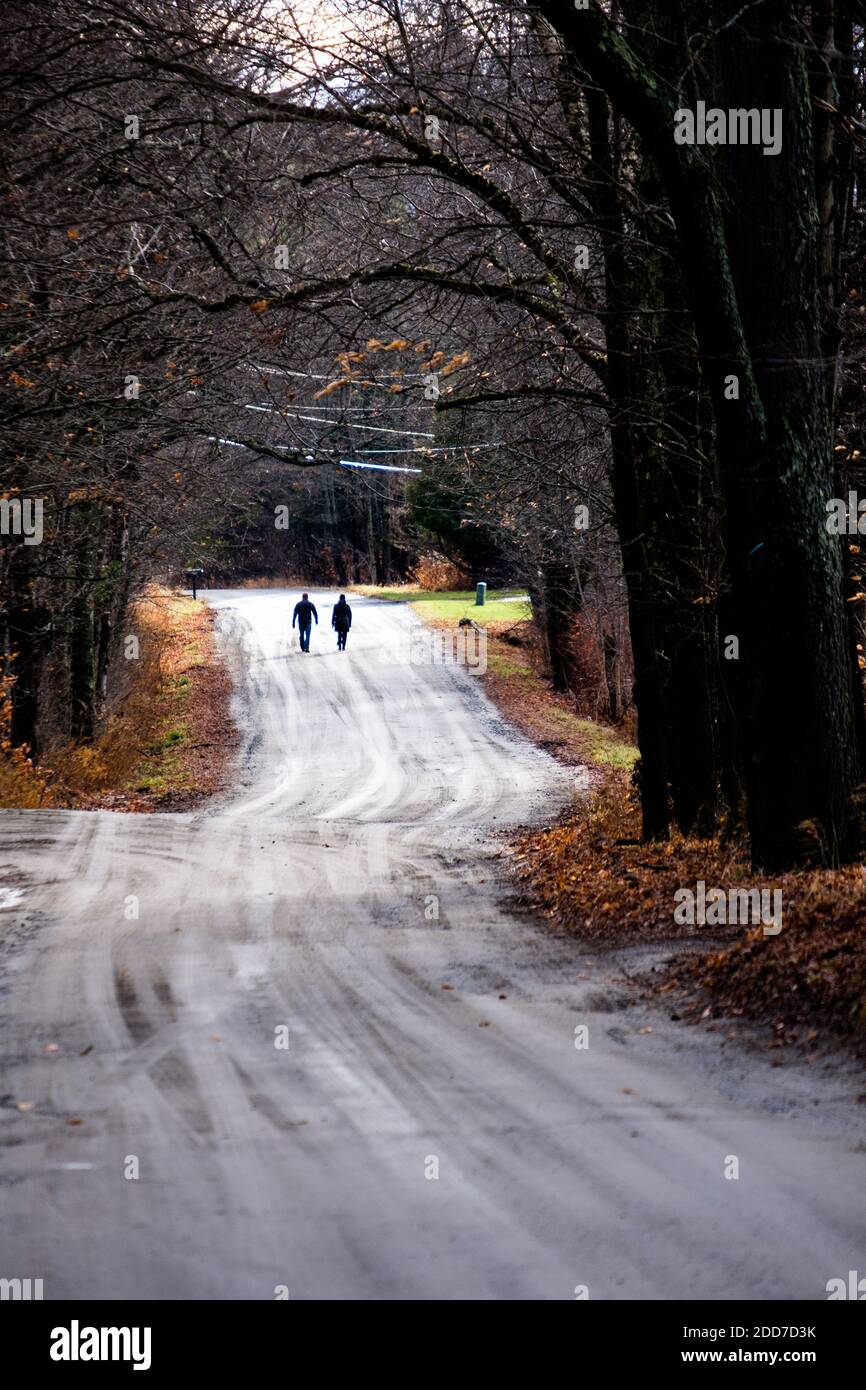 A couple are silhouetted as they walk on a rural dirt road, East Montpelier, VT, New England, USA. Stock Photo