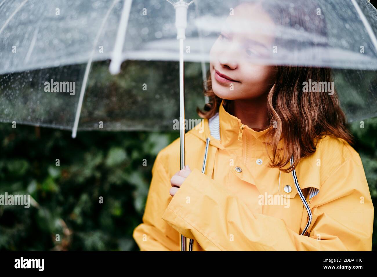 Girl in raincoat looking away while standing under umbrella outdoors Stock Photo