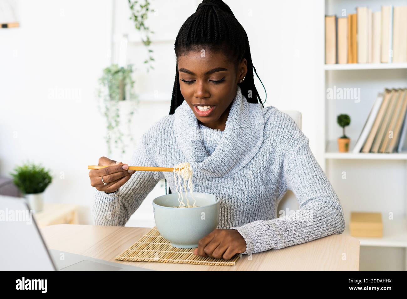Young woman eating noodles while sitting at home Stock Photo