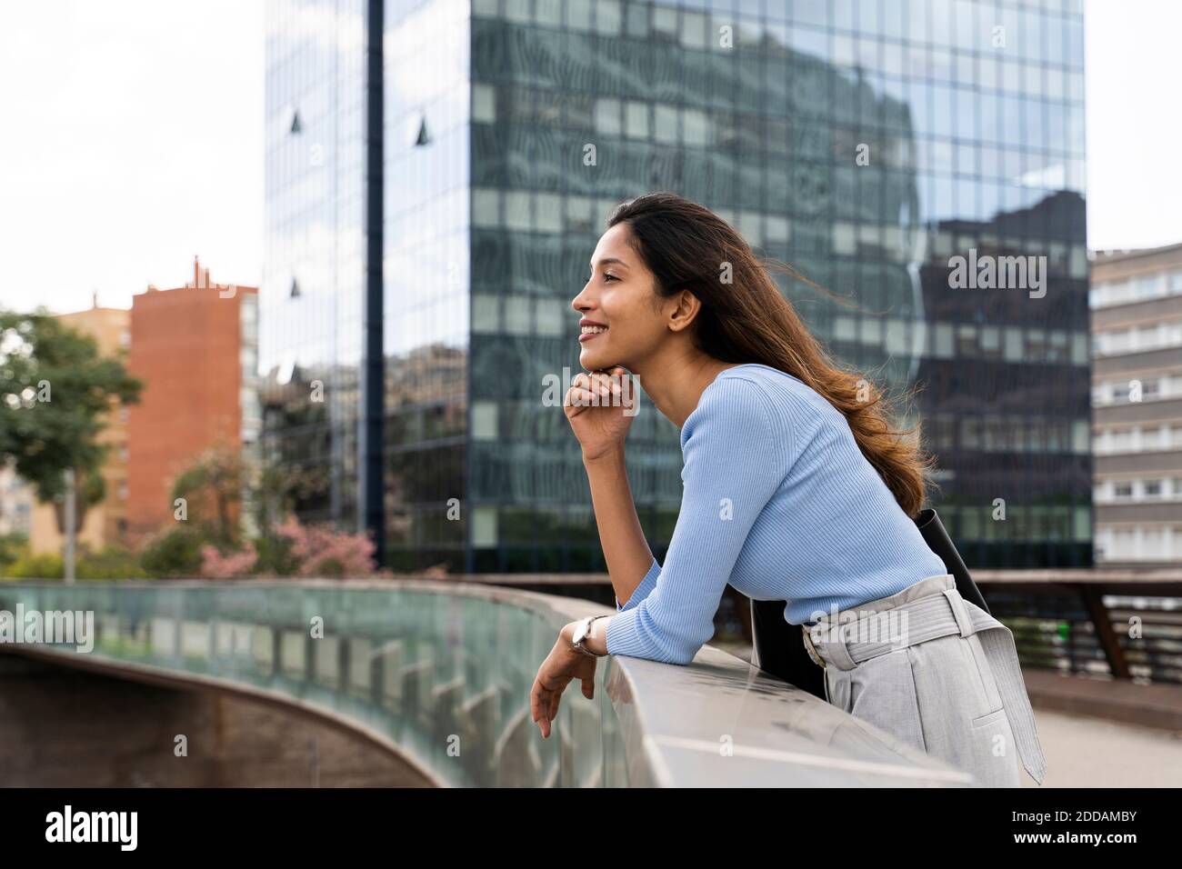 Thoughtful young businesswoman leaning on railing of footbridge Stock Photo