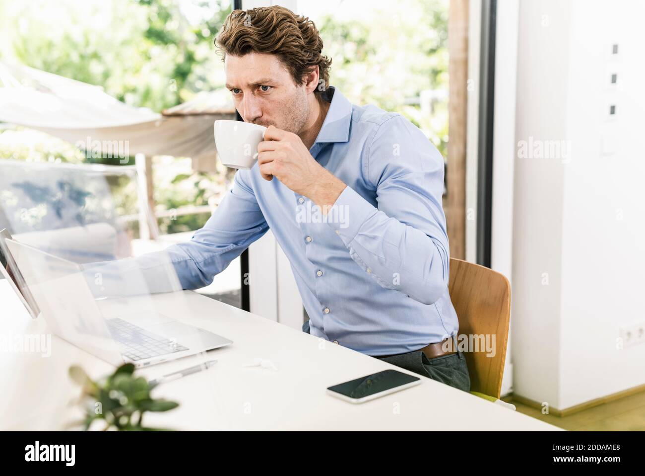 Man working on laptop while drinking coffee sitting in office Stock Photo