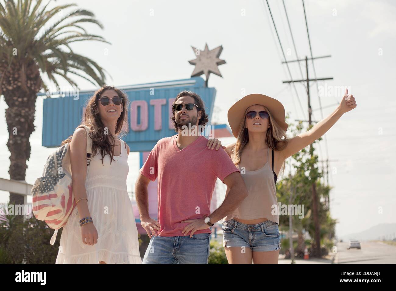 Male and female friends in sunglasses hailing a ride during sunny day Stock Photo
