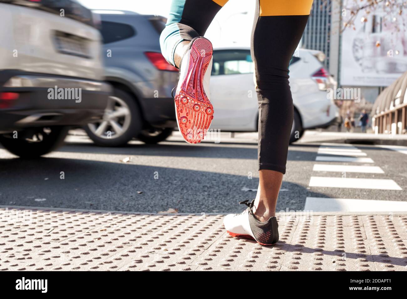 Young woman wearing sports shoe crossing road in traffic while running in city Stock Photo