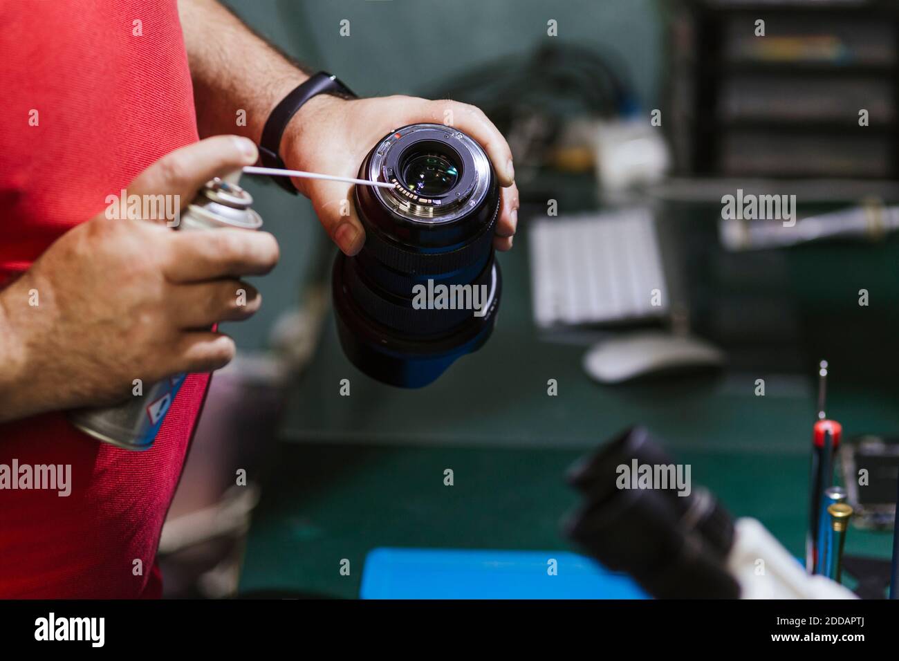 Repairman holding spray can and lens at electronics repair shop Stock Photo