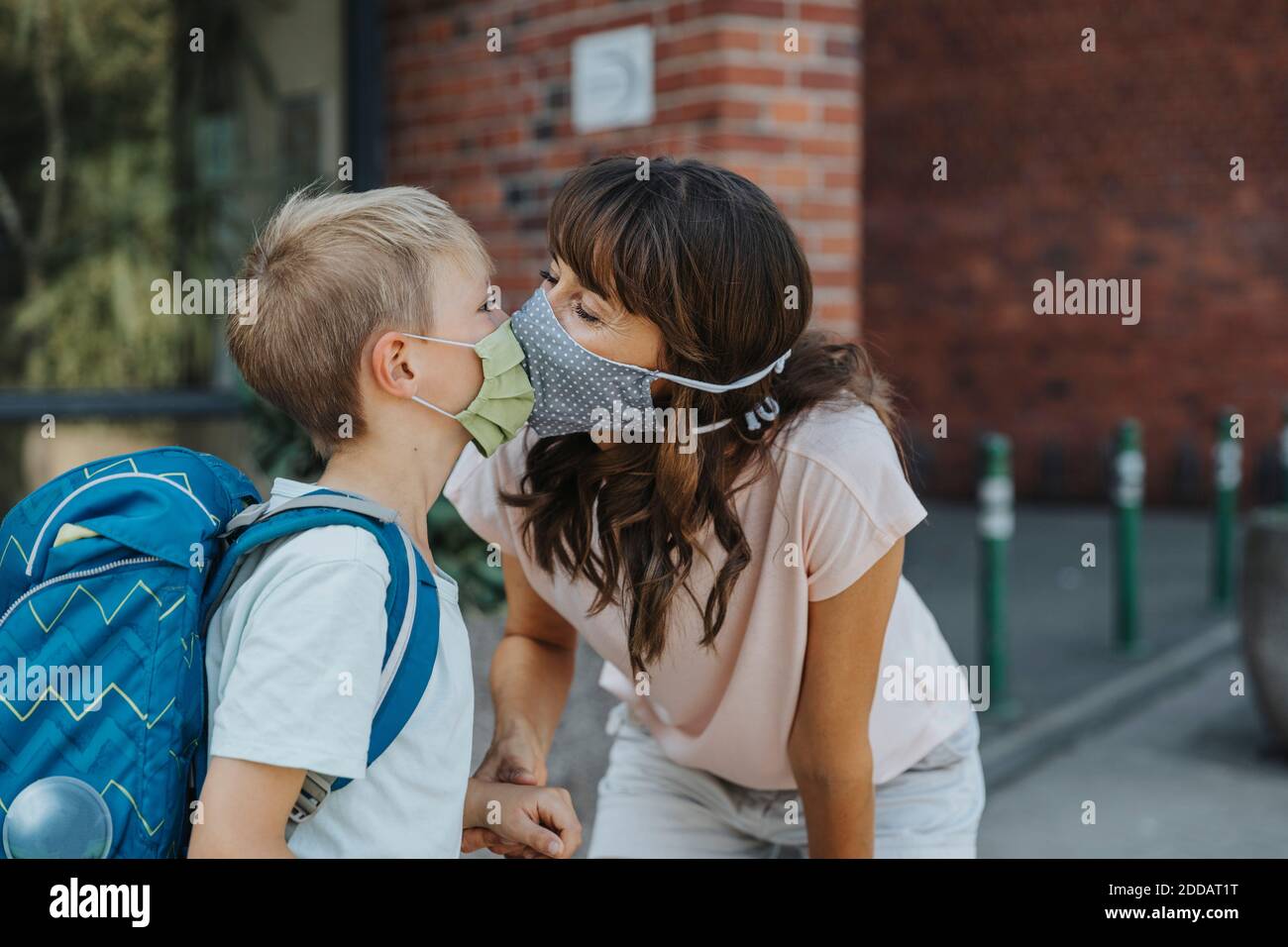 Mother kissing son wearing protective face mask standing in font of school Stock Photo